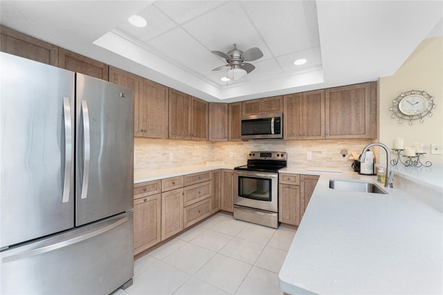 kitchen with tasteful backsplash, light countertops, a tray ceiling, stainless steel appliances, and a sink