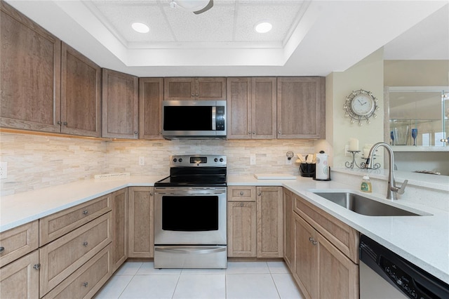 kitchen featuring a sink, tasteful backsplash, stainless steel appliances, light tile patterned floors, and a raised ceiling