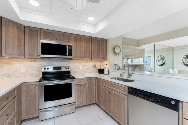 kitchen featuring a sink, backsplash, appliances with stainless steel finishes, light countertops, and a raised ceiling