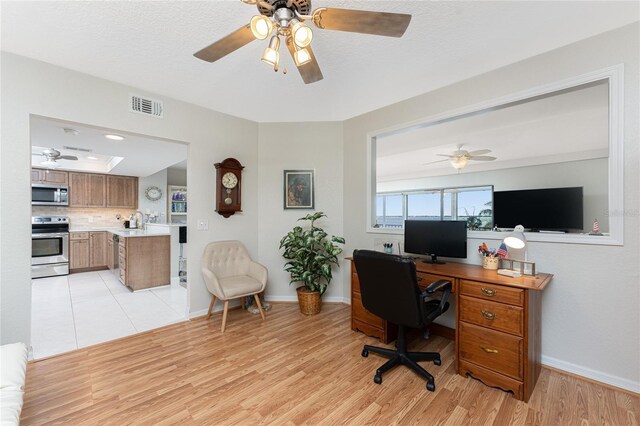 home office with baseboards, visible vents, light wood finished floors, ceiling fan, and a textured ceiling