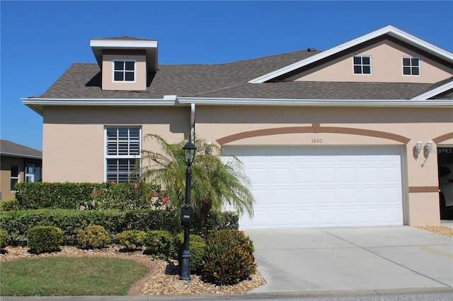 view of front facade featuring stucco siding, driveway, a shingled roof, and a garage