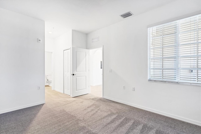 unfurnished bedroom featuring ensuite bath, carpet, visible vents, and baseboards