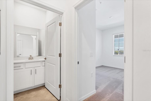 hall featuring light tile patterned floors, light colored carpet, baseboards, and a sink