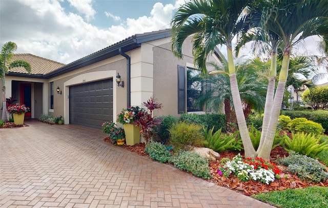 view of side of home with a tile roof, decorative driveway, an attached garage, and stucco siding