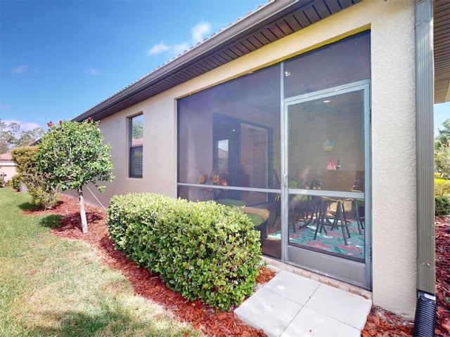 view of side of property featuring stucco siding, a lawn, and a sunroom