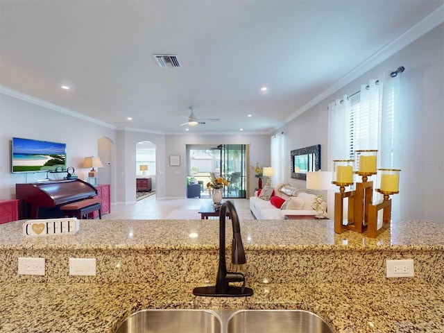 kitchen featuring open floor plan, ornamental molding, light stone counters, arched walkways, and a sink