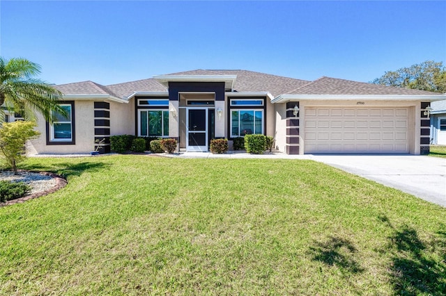 prairie-style home with stucco siding, a front yard, an attached garage, and driveway