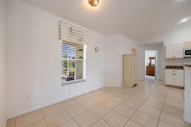 unfurnished room with lofted ceiling, light tile patterned floors, and baseboards