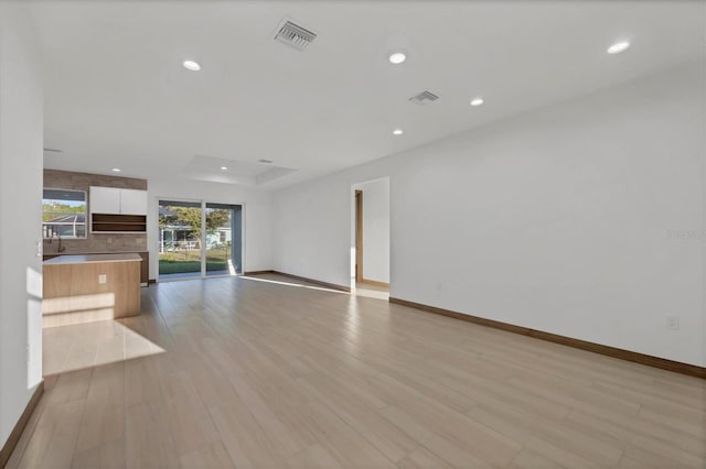 unfurnished living room with a tray ceiling, recessed lighting, light wood-style floors, and visible vents