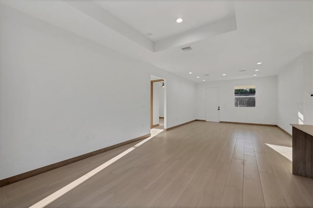 empty room featuring visible vents, light wood-style flooring, a tray ceiling, recessed lighting, and baseboards