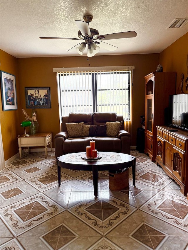 living room featuring light tile patterned floors, visible vents, a textured ceiling, and a ceiling fan