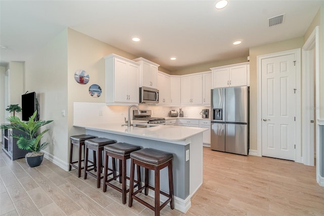 kitchen featuring visible vents, light wood finished floors, a peninsula, a sink, and stainless steel appliances