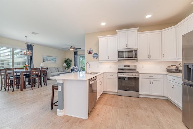 kitchen with a peninsula, light wood-style flooring, a sink, white cabinets, and appliances with stainless steel finishes