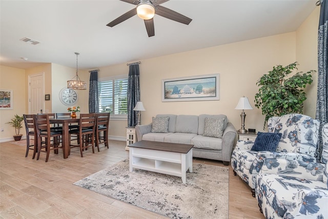 living area with ceiling fan with notable chandelier, visible vents, light wood finished floors, and baseboards