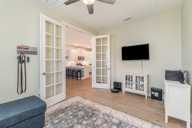 interior space with a ceiling fan, light wood-style flooring, french doors, and visible vents