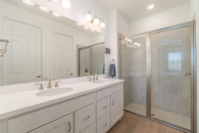 bathroom with a shower stall, wood finished floors, double vanity, and a sink