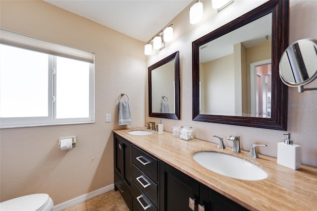 bathroom with a sink, baseboards, toilet, and double vanity