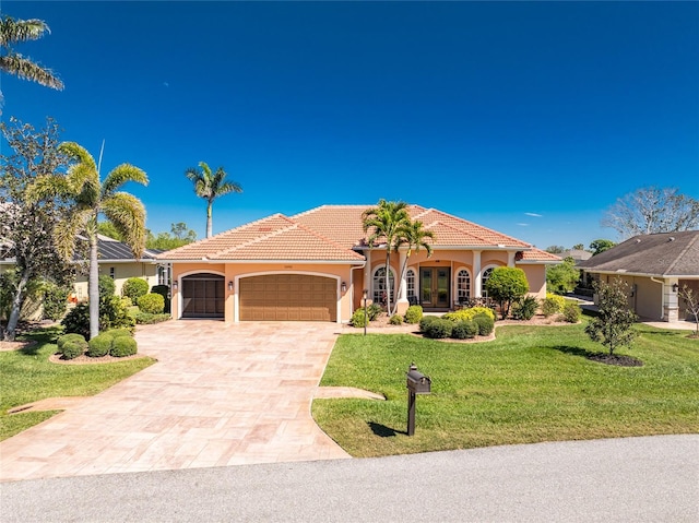 mediterranean / spanish home with a front yard, french doors, a garage, a tiled roof, and decorative driveway