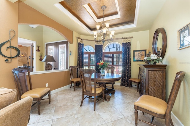 dining area with baseboards, a tray ceiling, ornamental molding, an inviting chandelier, and arched walkways