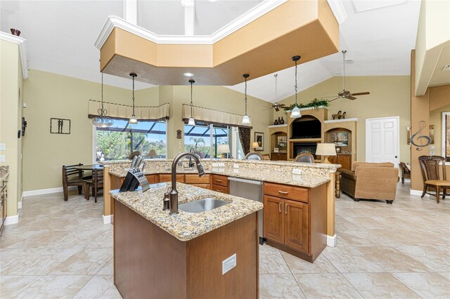 kitchen featuring light stone countertops, a center island with sink, brown cabinets, a ceiling fan, and a sink