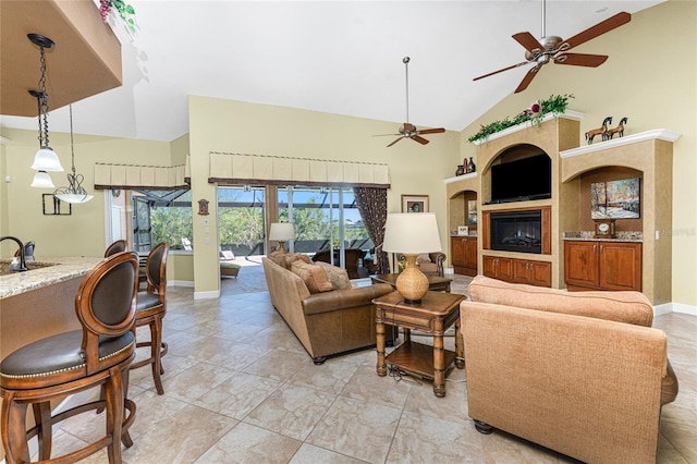 living area with a glass covered fireplace, ceiling fan, baseboards, and high vaulted ceiling