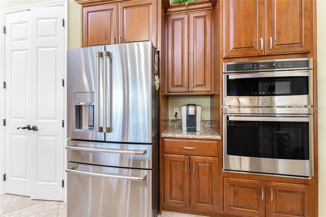 kitchen with stainless steel appliances, light stone countertops, brown cabinets, and light tile patterned flooring