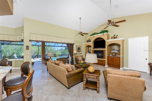 living area featuring a ceiling fan, baseboards, visible vents, high vaulted ceiling, and a glass covered fireplace