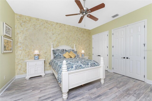 bedroom with visible vents, baseboards, wood finished floors, and wallpapered walls