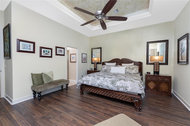 bedroom featuring a tray ceiling, wood finished floors, visible vents, and baseboards