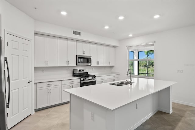 kitchen featuring visible vents, an island with sink, a sink, stainless steel appliances, and white cabinets