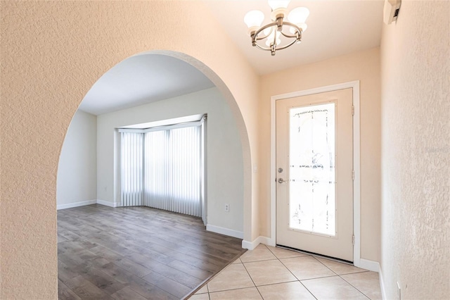 entryway with baseboards, arched walkways, a chandelier, and a textured wall