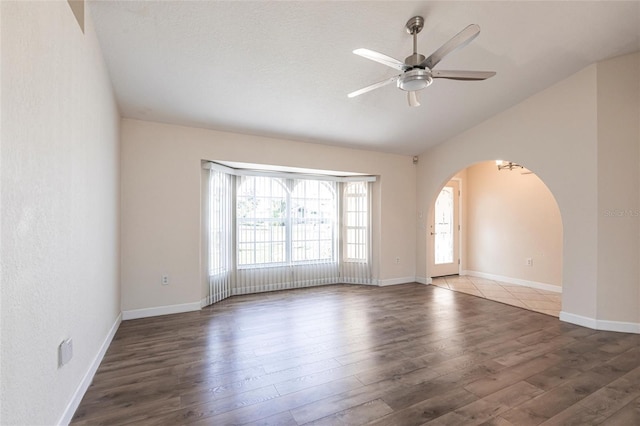 unfurnished room featuring baseboards, lofted ceiling, wood finished floors, arched walkways, and a ceiling fan