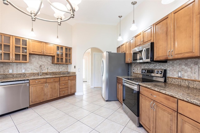 kitchen featuring light tile patterned flooring, arched walkways, a sink, stainless steel appliances, and brown cabinets