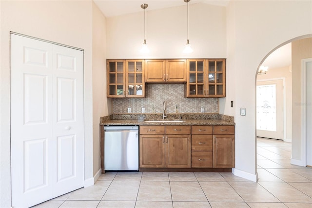 kitchen with light tile patterned floors, brown cabinetry, arched walkways, a sink, and dishwasher