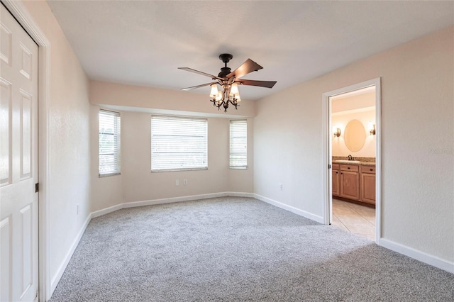 unfurnished bedroom with baseboards, ensuite bath, ceiling fan, a sink, and light colored carpet