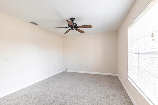 carpeted spare room with a wealth of natural light, visible vents, ceiling fan, and baseboards