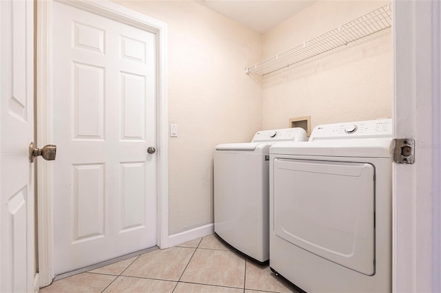 clothes washing area featuring washer and dryer, laundry area, light tile patterned flooring, and baseboards