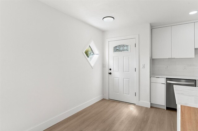 kitchen with light wood finished floors, backsplash, baseboards, dishwasher, and white cabinets