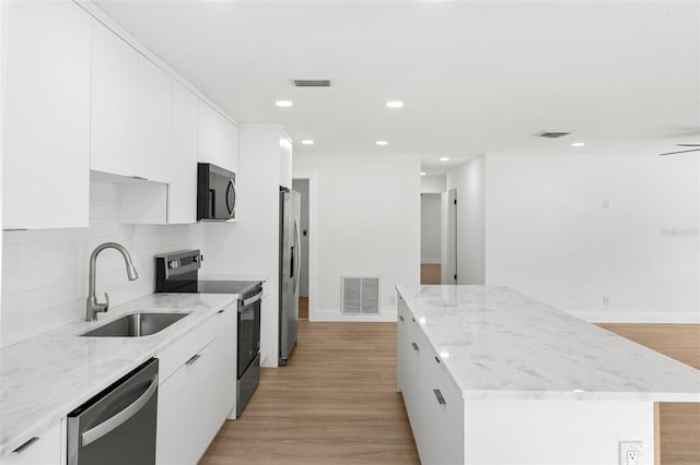 kitchen featuring visible vents, a sink, stainless steel appliances, white cabinets, and a center island