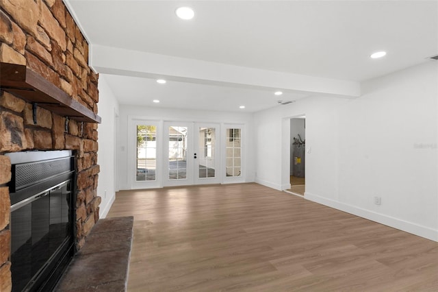 unfurnished living room with a stone fireplace, recessed lighting, french doors, and wood finished floors