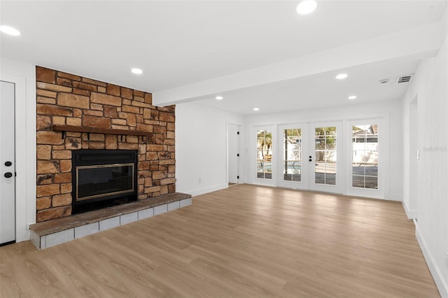 unfurnished living room with a stone fireplace, recessed lighting, french doors, and light wood-style floors