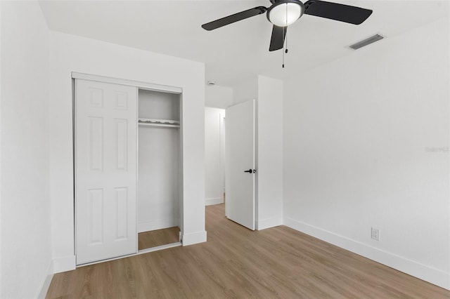 unfurnished bedroom with wood finished floors, visible vents, a closet, and baseboards