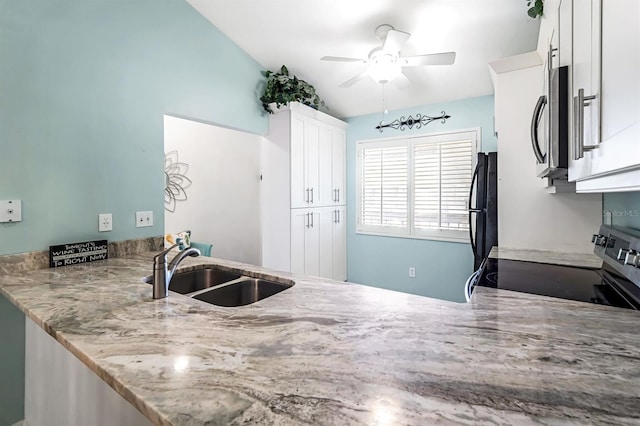 kitchen with light stone counters, a peninsula, a sink, stainless steel appliances, and white cabinetry