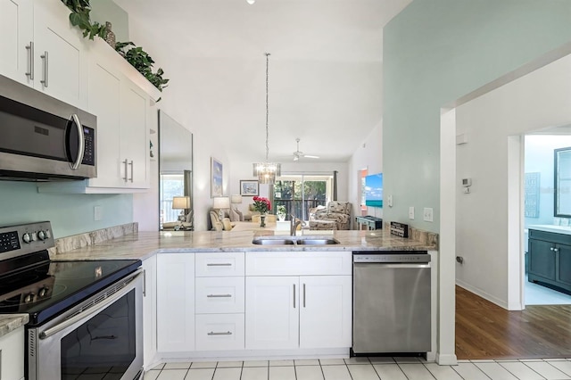 kitchen with a sink, white cabinets, appliances with stainless steel finishes, open floor plan, and a chandelier