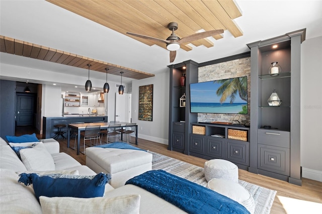 living room featuring baseboards, built in shelves, a ceiling fan, and light wood-style floors