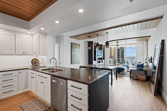 kitchen with dark countertops, light wood finished floors, a peninsula, stainless steel dishwasher, and a sink