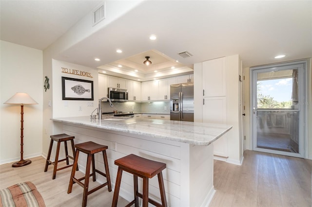 kitchen featuring a kitchen bar, white cabinetry, stainless steel appliances, a peninsula, and light wood finished floors