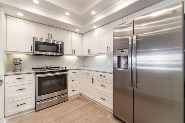 kitchen featuring a tray ceiling, appliances with stainless steel finishes, ornamental molding, and white cabinetry