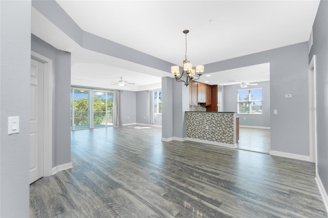 unfurnished living room with ceiling fan with notable chandelier, baseboards, and dark wood-style flooring