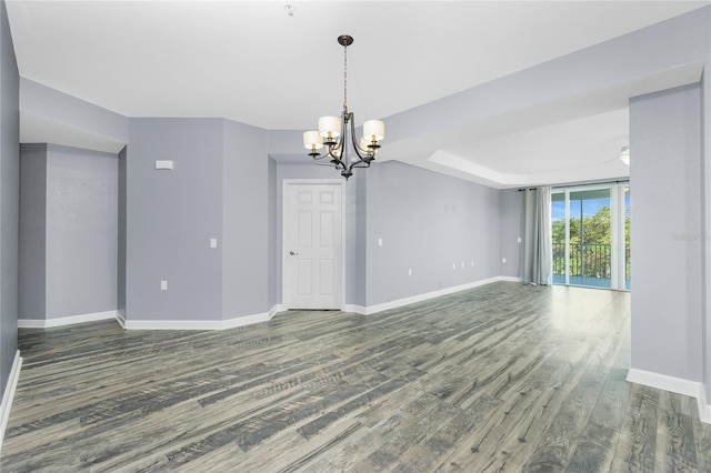 empty room featuring an inviting chandelier, a tray ceiling, baseboards, and wood finished floors